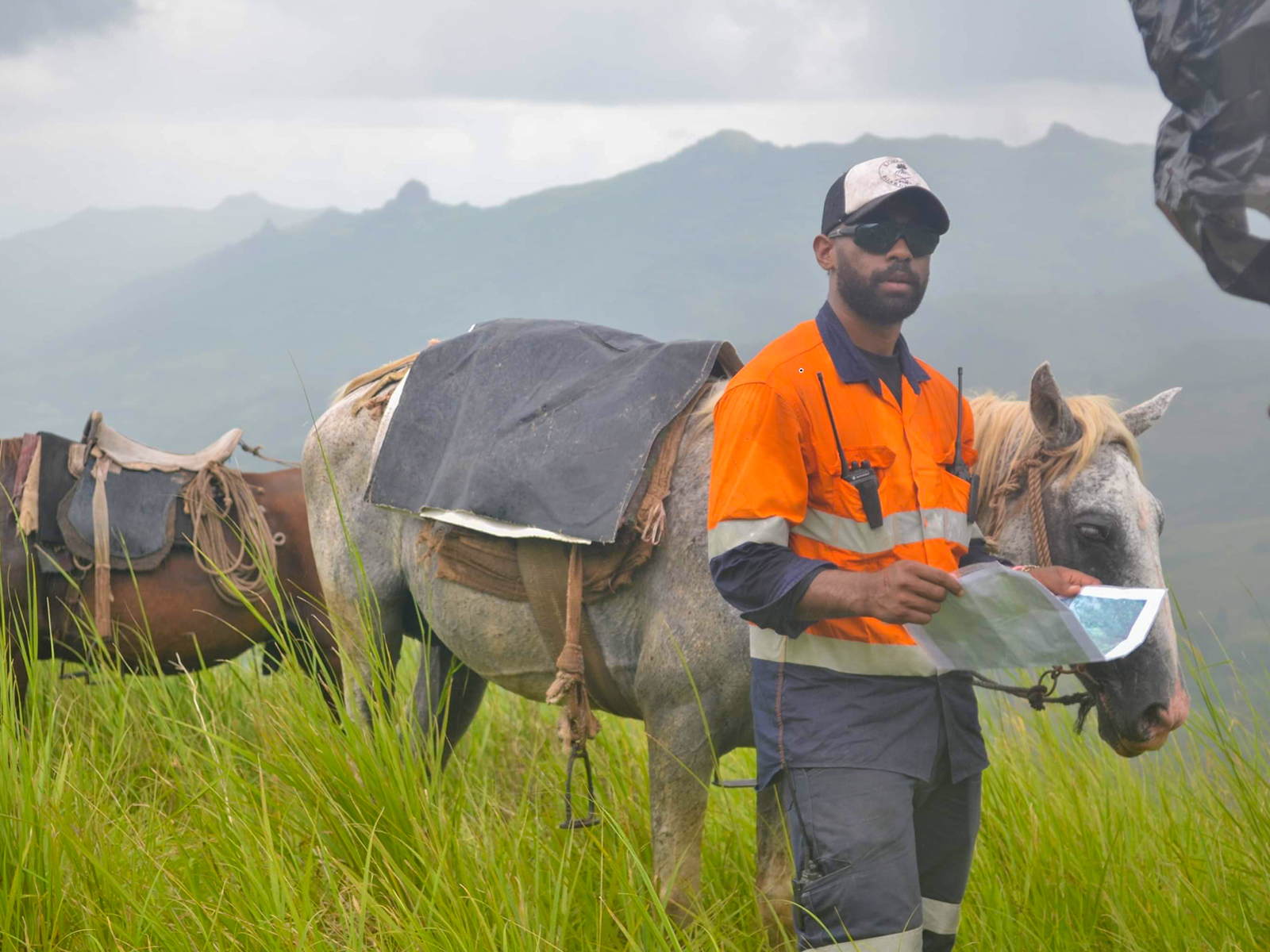 Man with map in the mountains with horse behind him